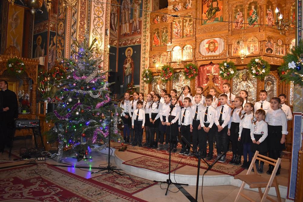 A group of children in white and black matching outfits gather at the front of an elaborate church to sing as a choir at Christmastime.