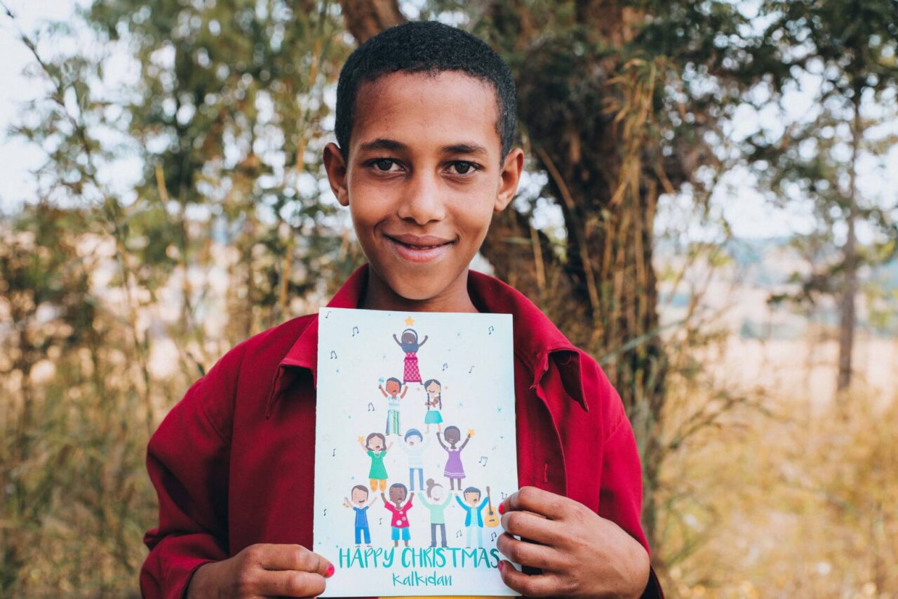 A boy in Ethiopia is holding a Christmas card and looking into the camera.