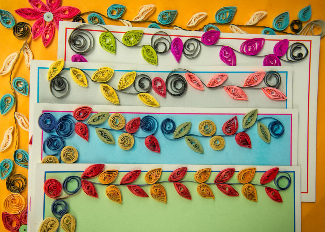 Colorful sheets of paper decorated with vines and flowers from coils of paper are laid out on display.