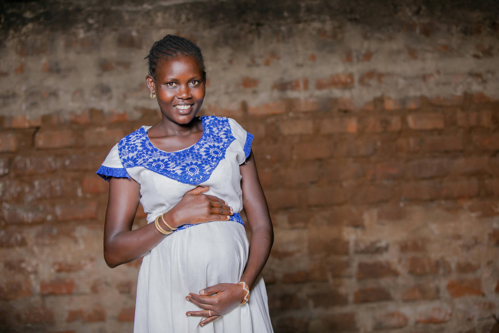 A pregnant Kenyan woman holds her stomach and smiles.