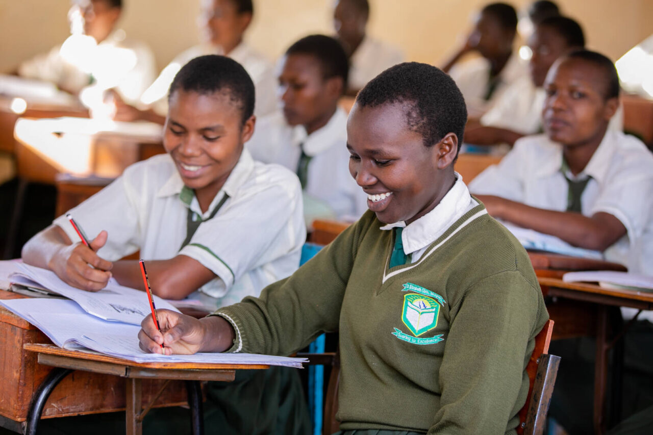 Teenage students wearing green uniforms in a classroom look at their schoolwork.