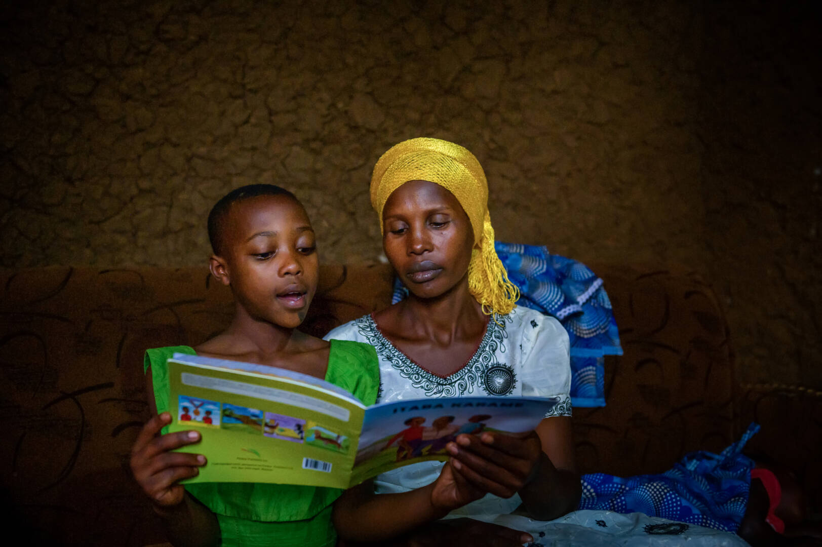 Dativa listens to Keza read a book that came from the World Vision&rsquo;s reading camp Keza attends.