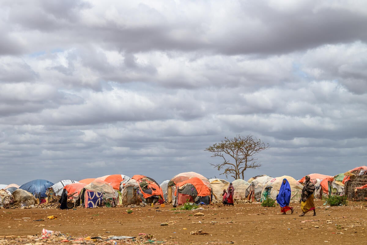Two women pass in front of makeshift tents in a displacement camp.