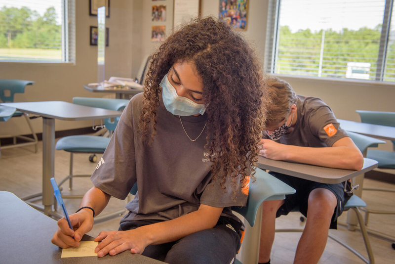 A student sits at a school desk and writes.