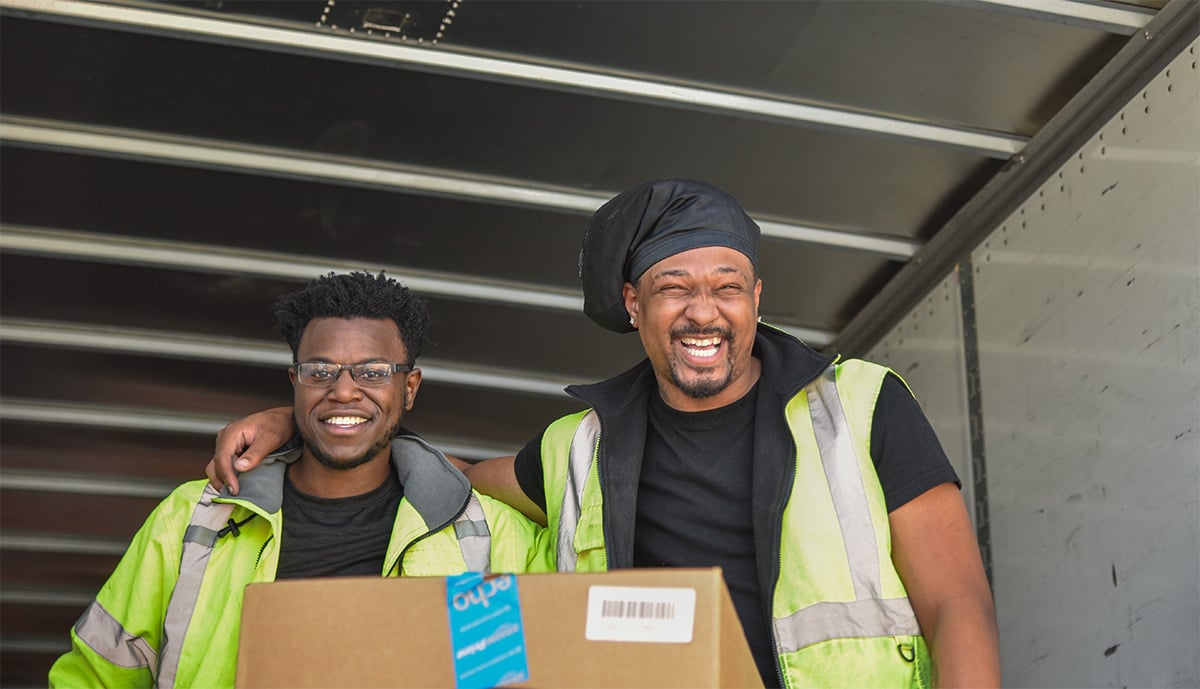two men smiling handing out boxes