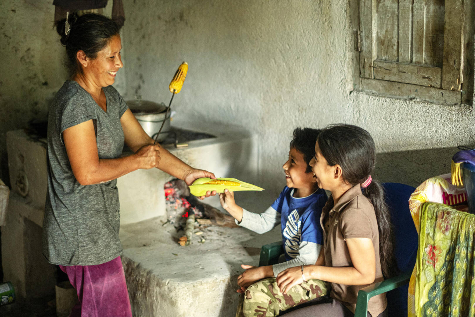 A mother hands her two children a stalk of roasted maize to share.