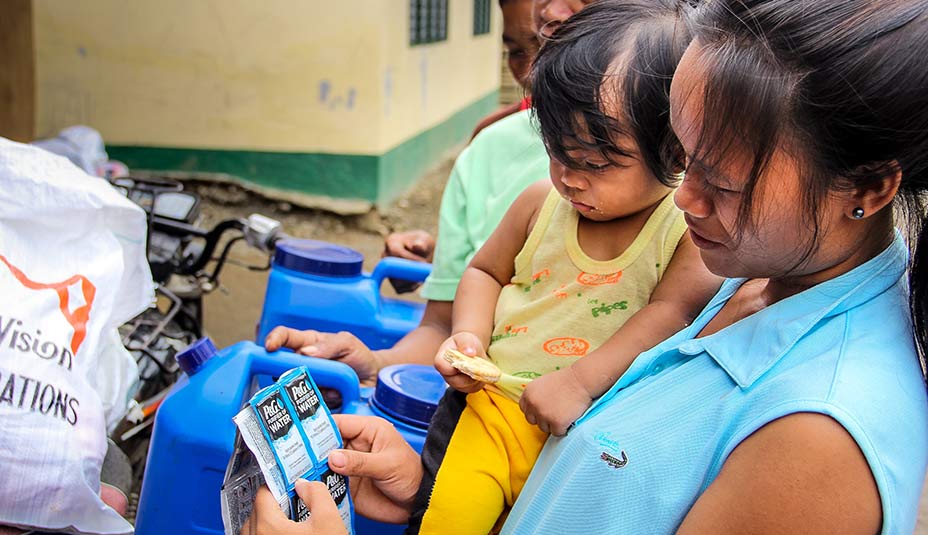 Woman holding her baby, and a couple P&G water purifier packets.