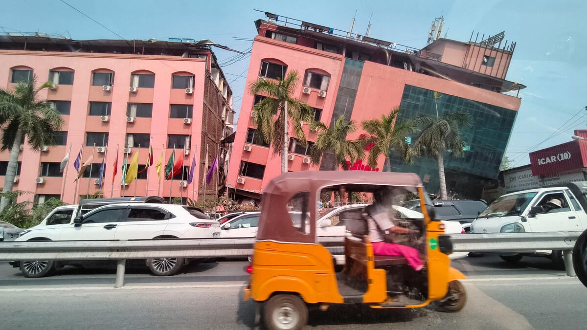 Motorists ride past pink-colored buildings, one seen tilting on its side, after a 7.7 magnitude earthquake in Myanmar.