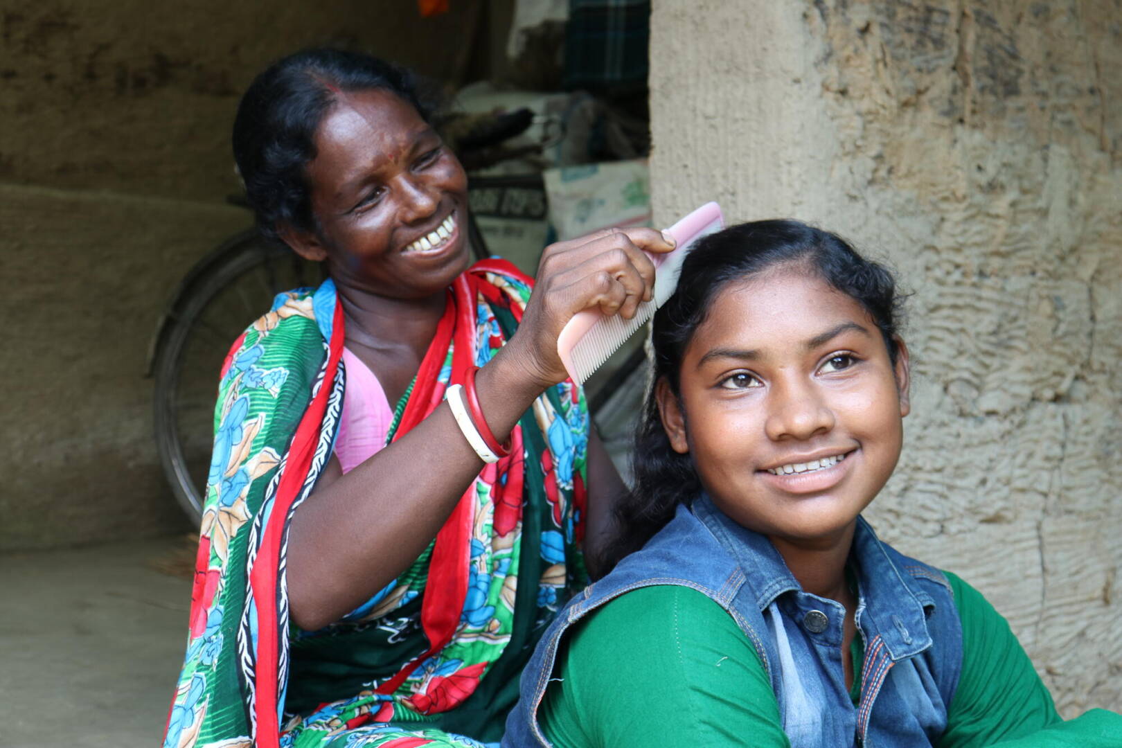 A mother smiles while she combs her daughter&rsquo;s hair.