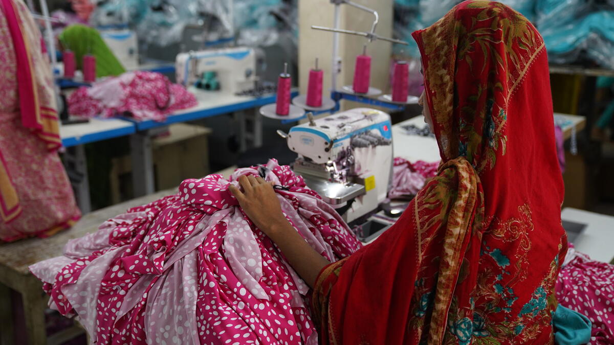 A girl, obscured by a red veil, sits at a sewing machine at a garment factory.