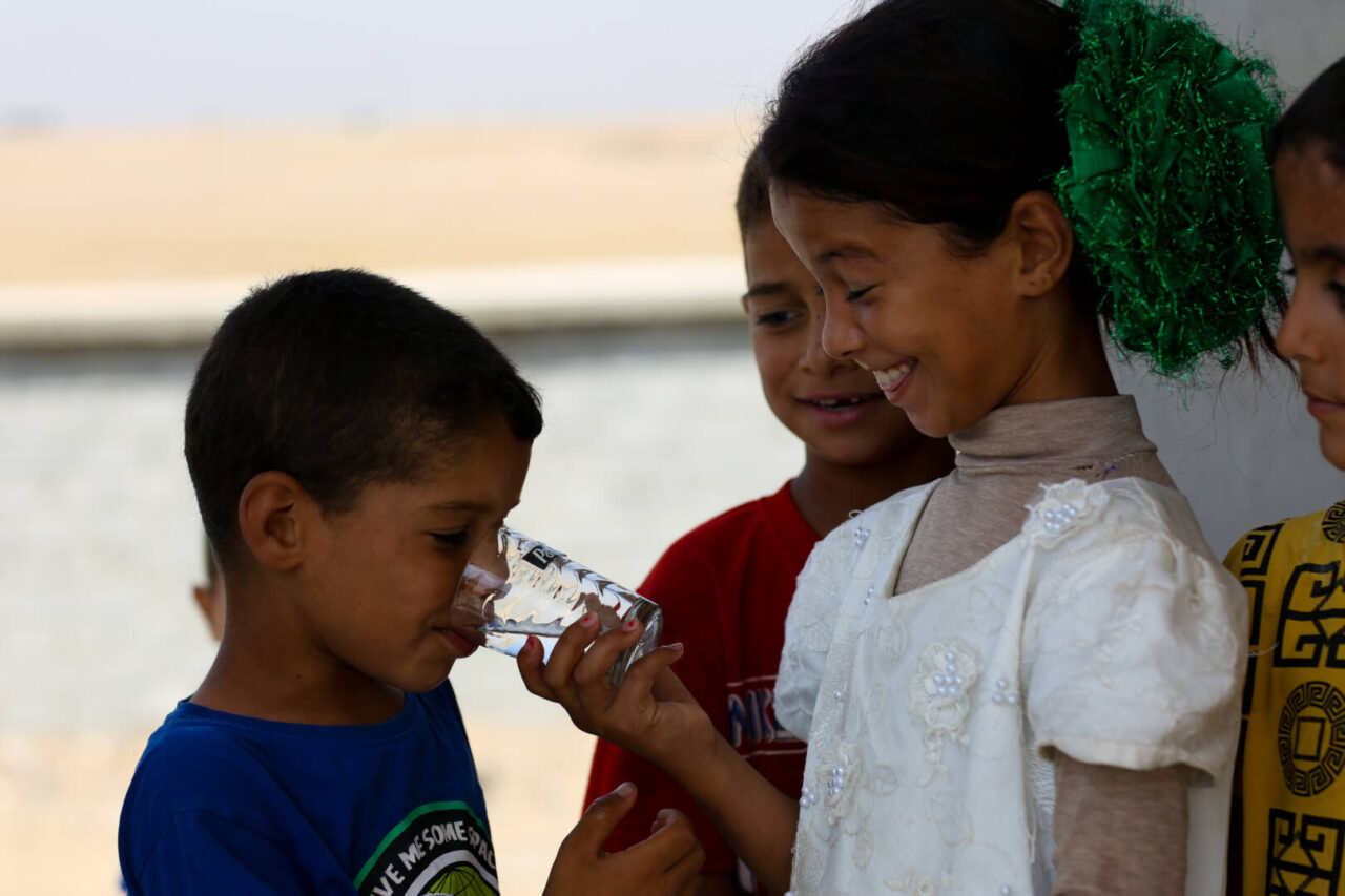 In Iraq, 12-year-old Aysha giggles while giving her cousin clean water to drink. 