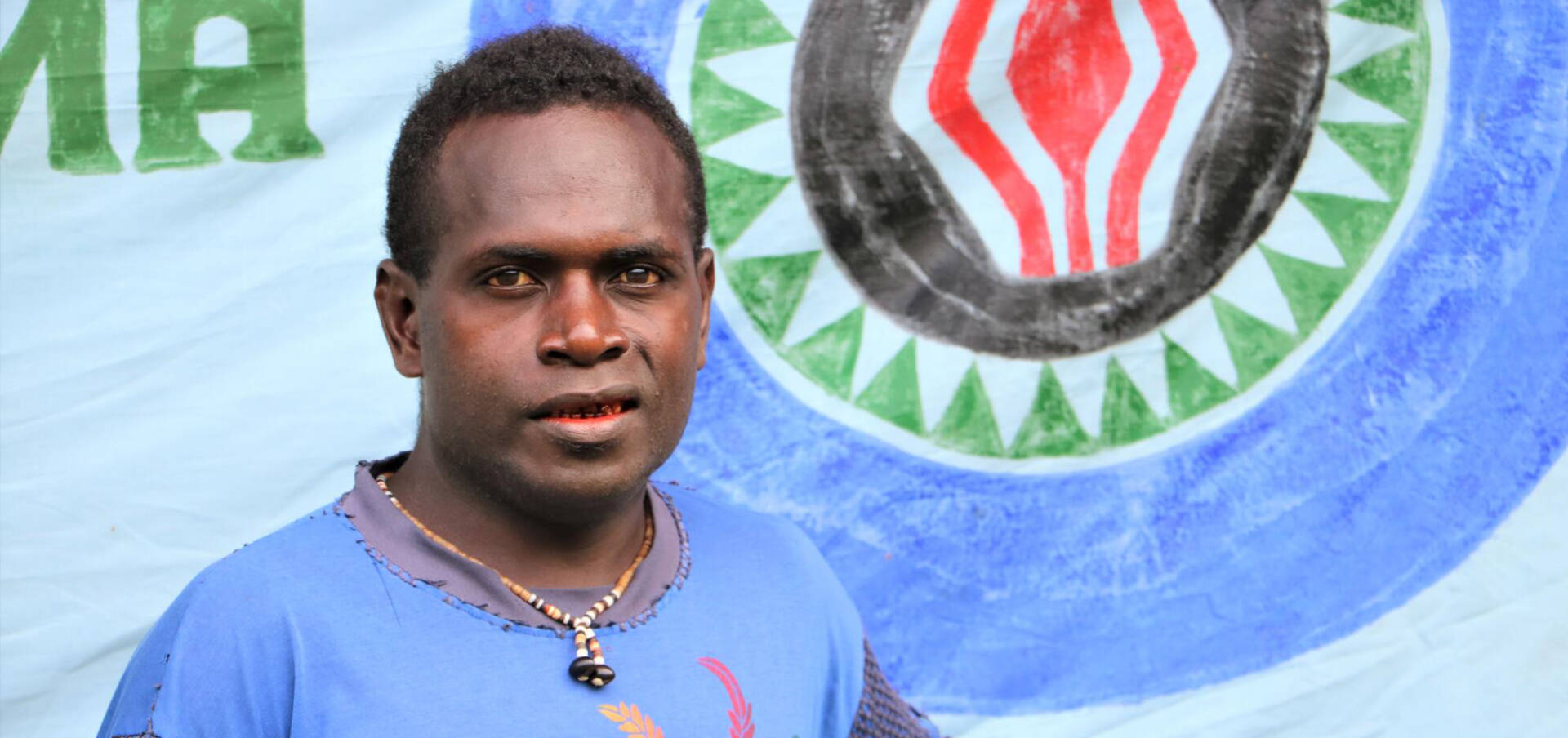 A Papua New Guinean man in a blue T-shirt looks to the camera.