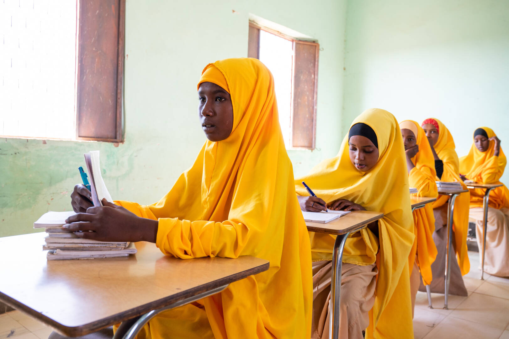 Girls dressed in traditional yellow Somali garments concentrate at their desks in a rural school.