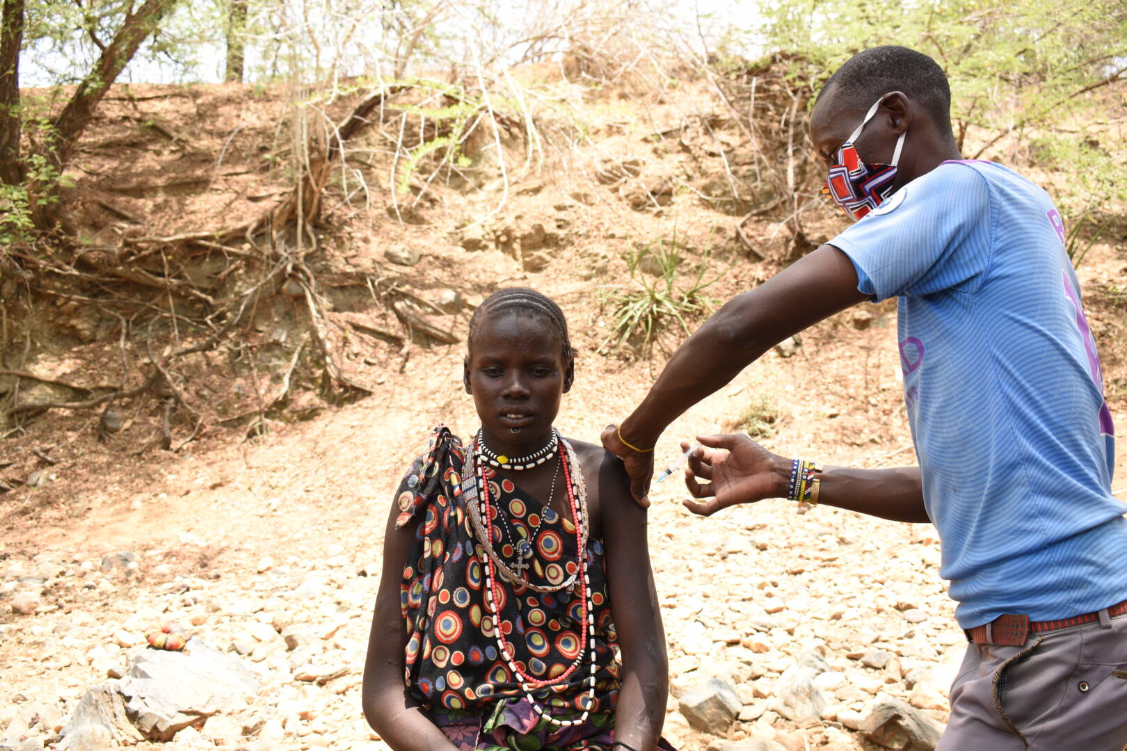 A woman in South Sudan sits and gets a vaccine from a man wearing a mask.