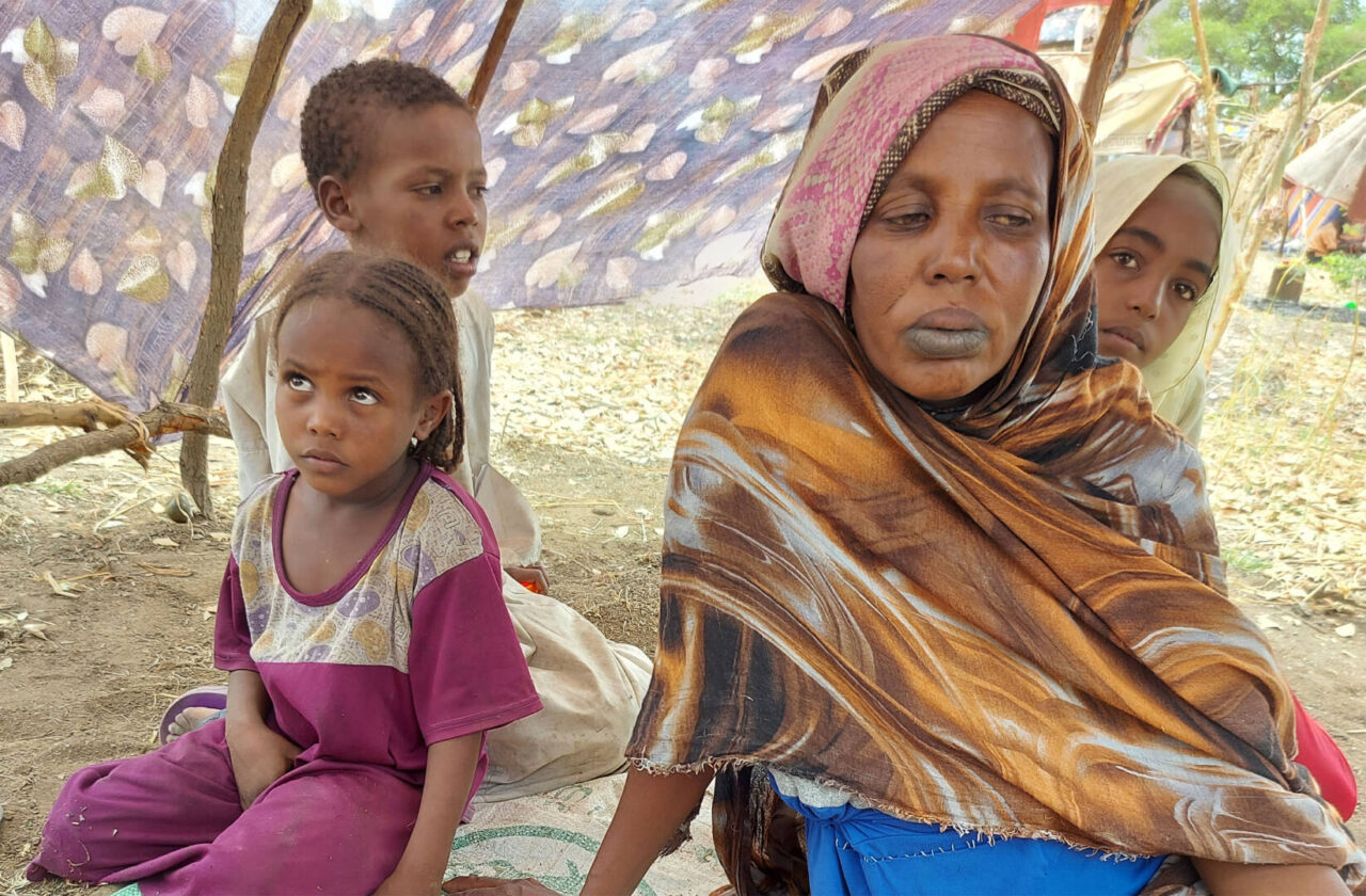 A mother glances wearily to the side as she and her three children sit under a makeshift tent in South Sudan.