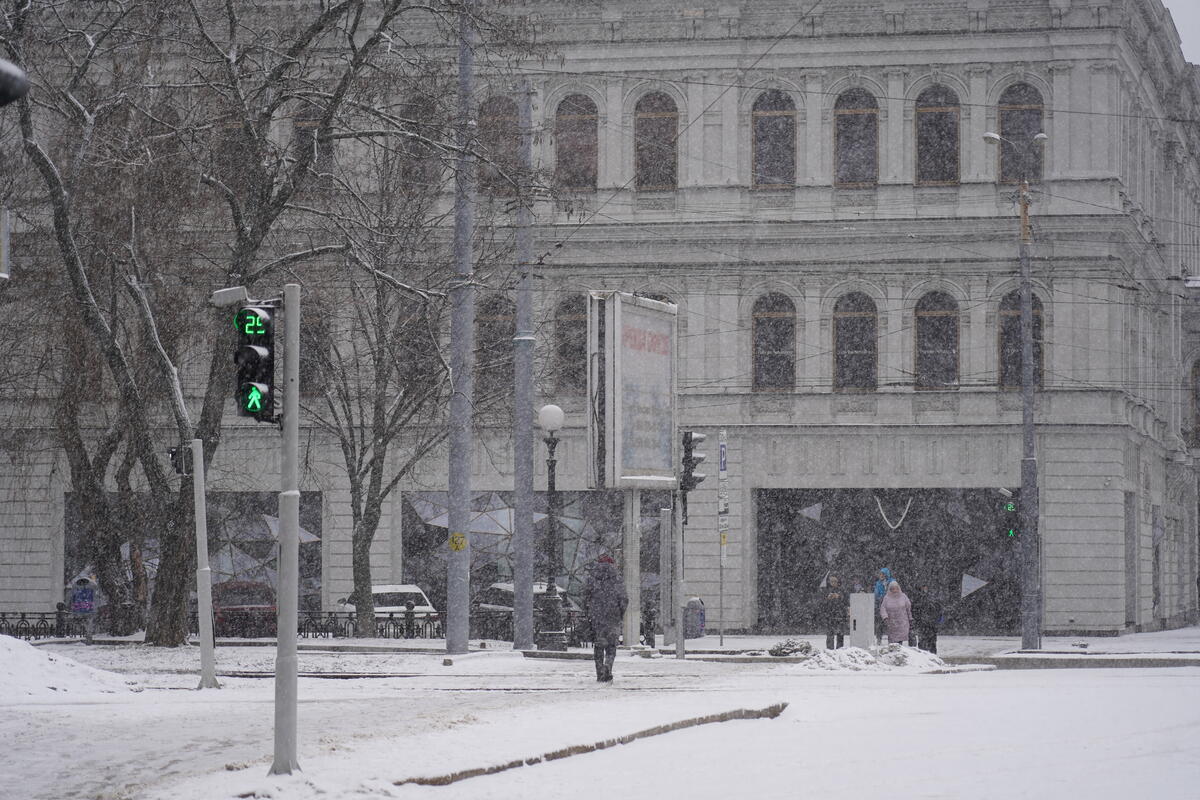 A winter scene in Dnipro, eastern Ukraine, with people bundled in coats crossing a city street amid snow flurries.