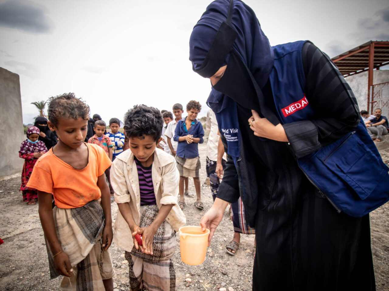 Children line up outside to practice handwashing instructions led by a humanitarian aid worker.