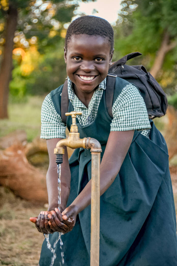 With a water tap installed by World Vision, water pours into Juliet&rsquo;s hands.