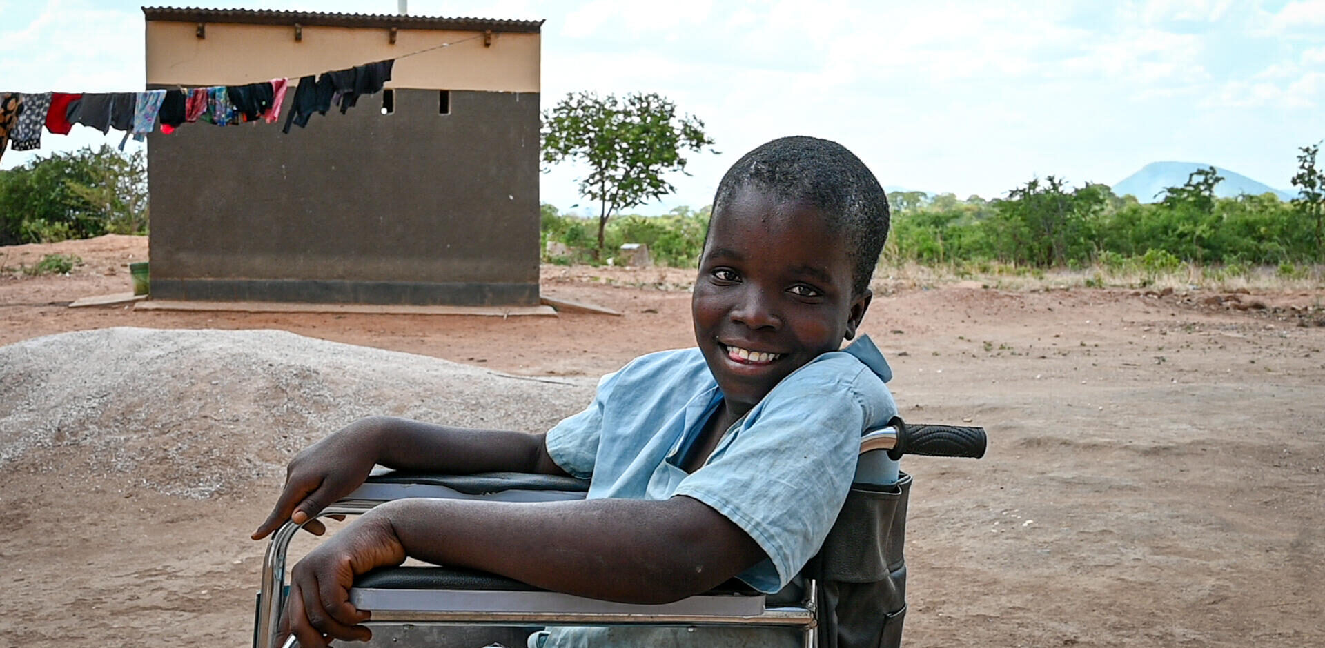 A Zambian girl smiles at the camera while she sits in her wheelchair.