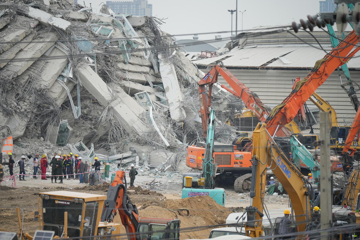 Rescue workers gather near massive piles of rubble and debris as earthmovers clear the destruction left by an earthquake.