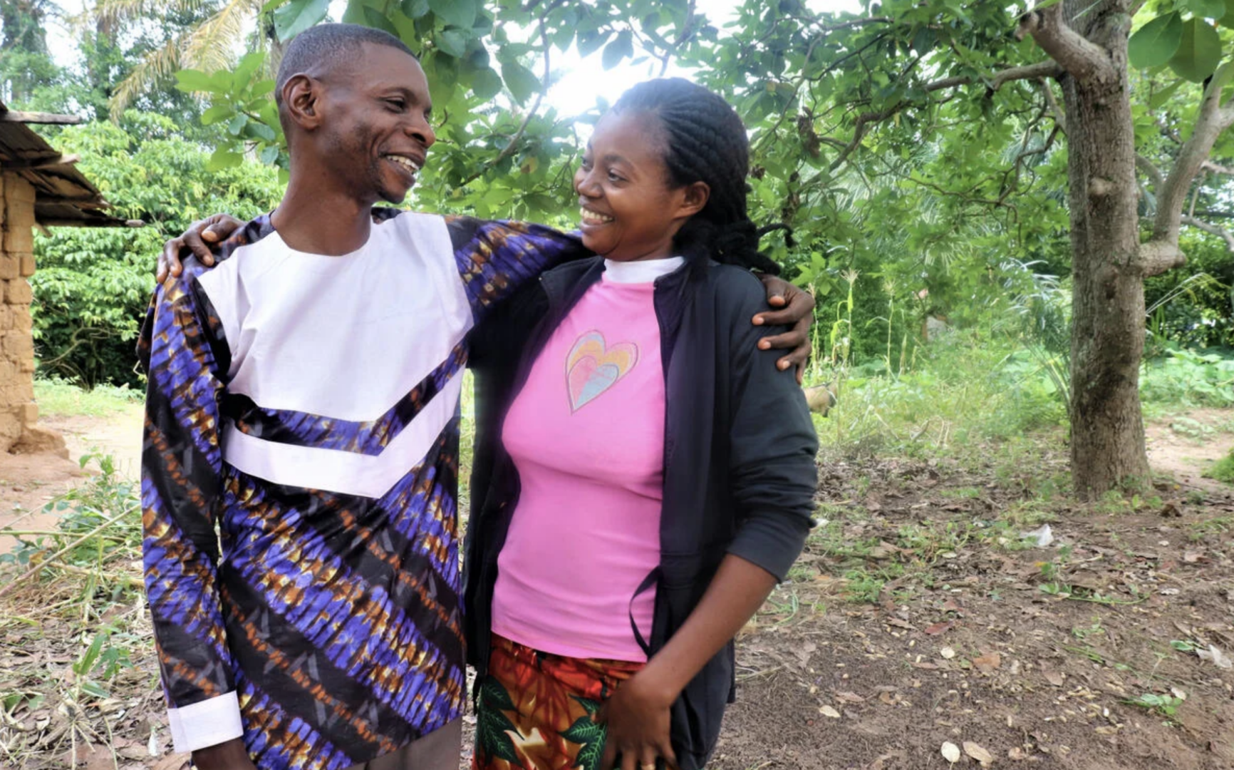 A happy couple embrace, smiling at each other, surrounded by lush greenery.
